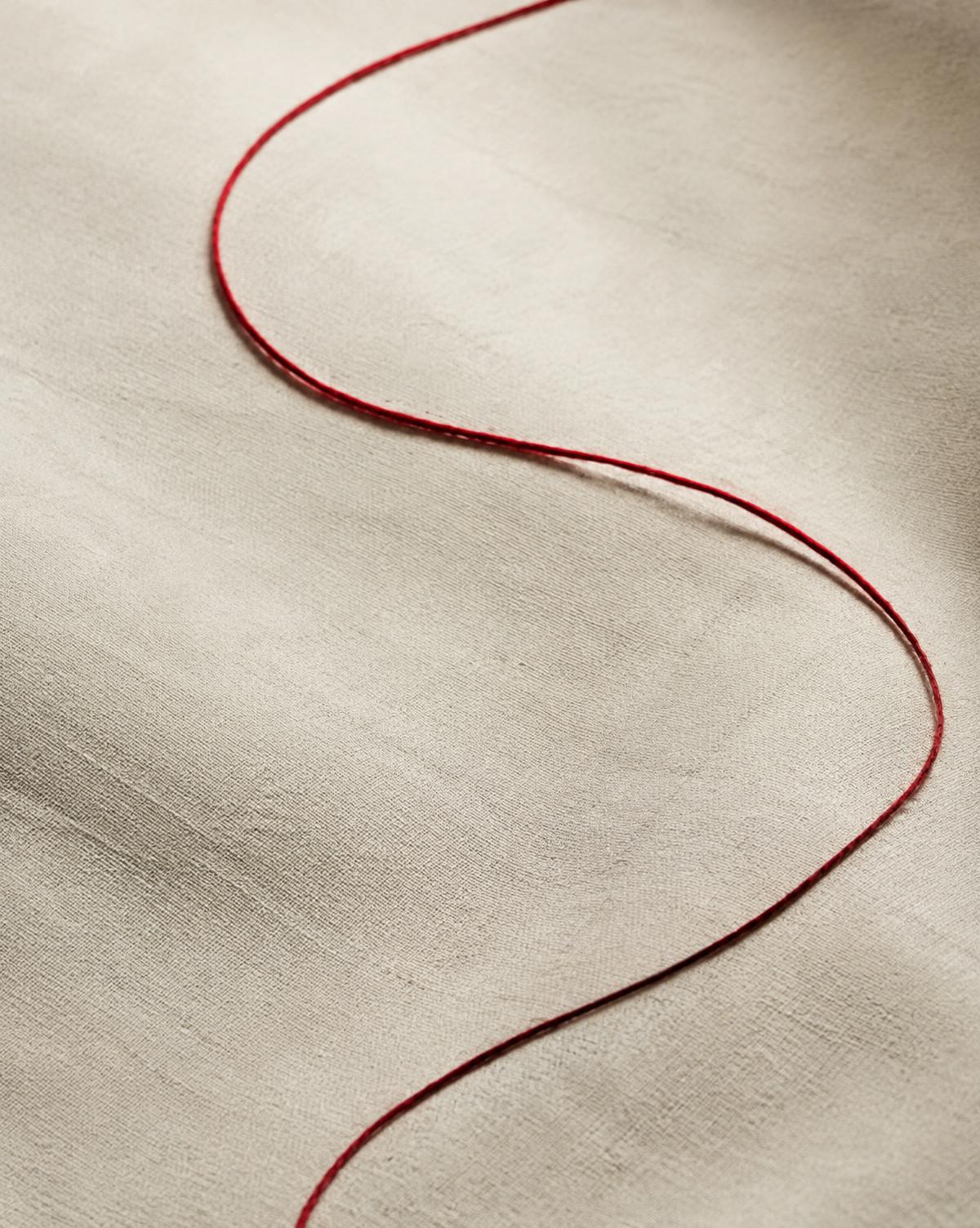 A single crimson thread curving across ivory linen